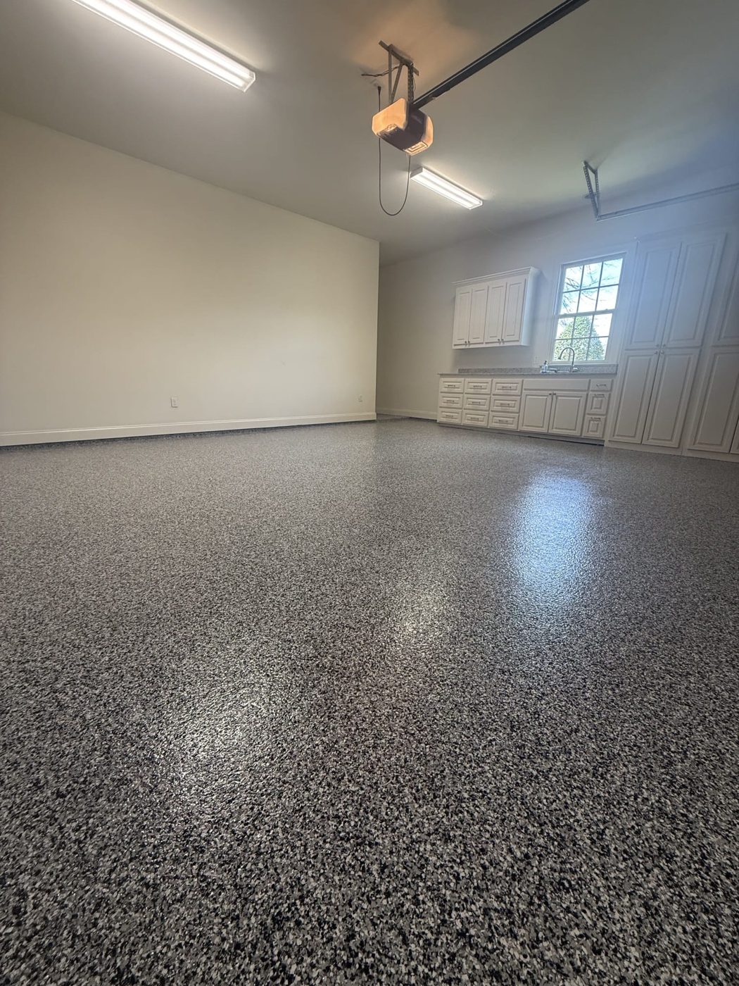 Large garage with white cabinets and a sink under a window, dark gray flake floor, garage door opener on the ceiling in Shenandoah, LA