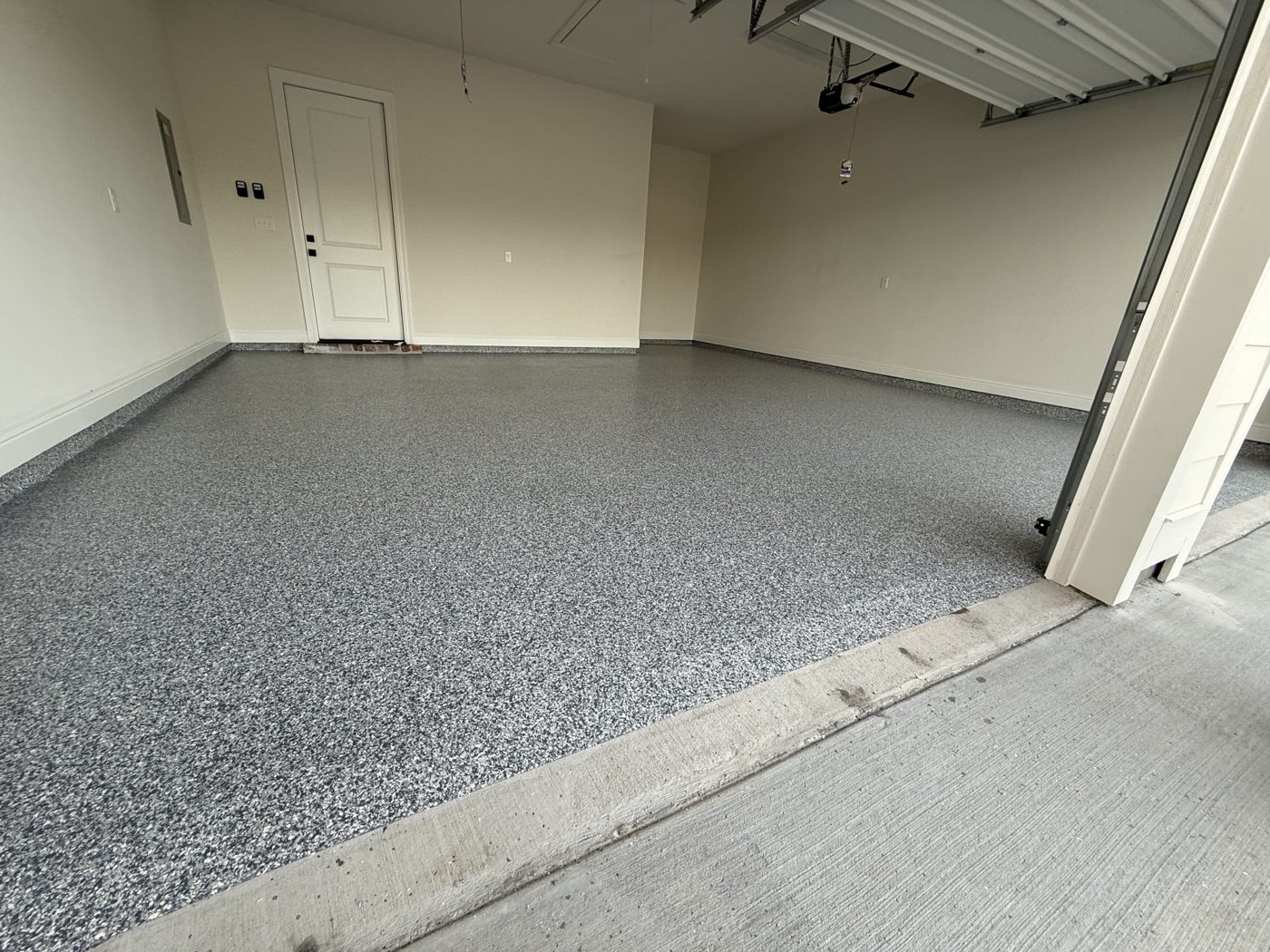 Two-car garage with the overhead door open, gray, black and white flake floor ending at the concrete driveway apron in Shenandoah, LA