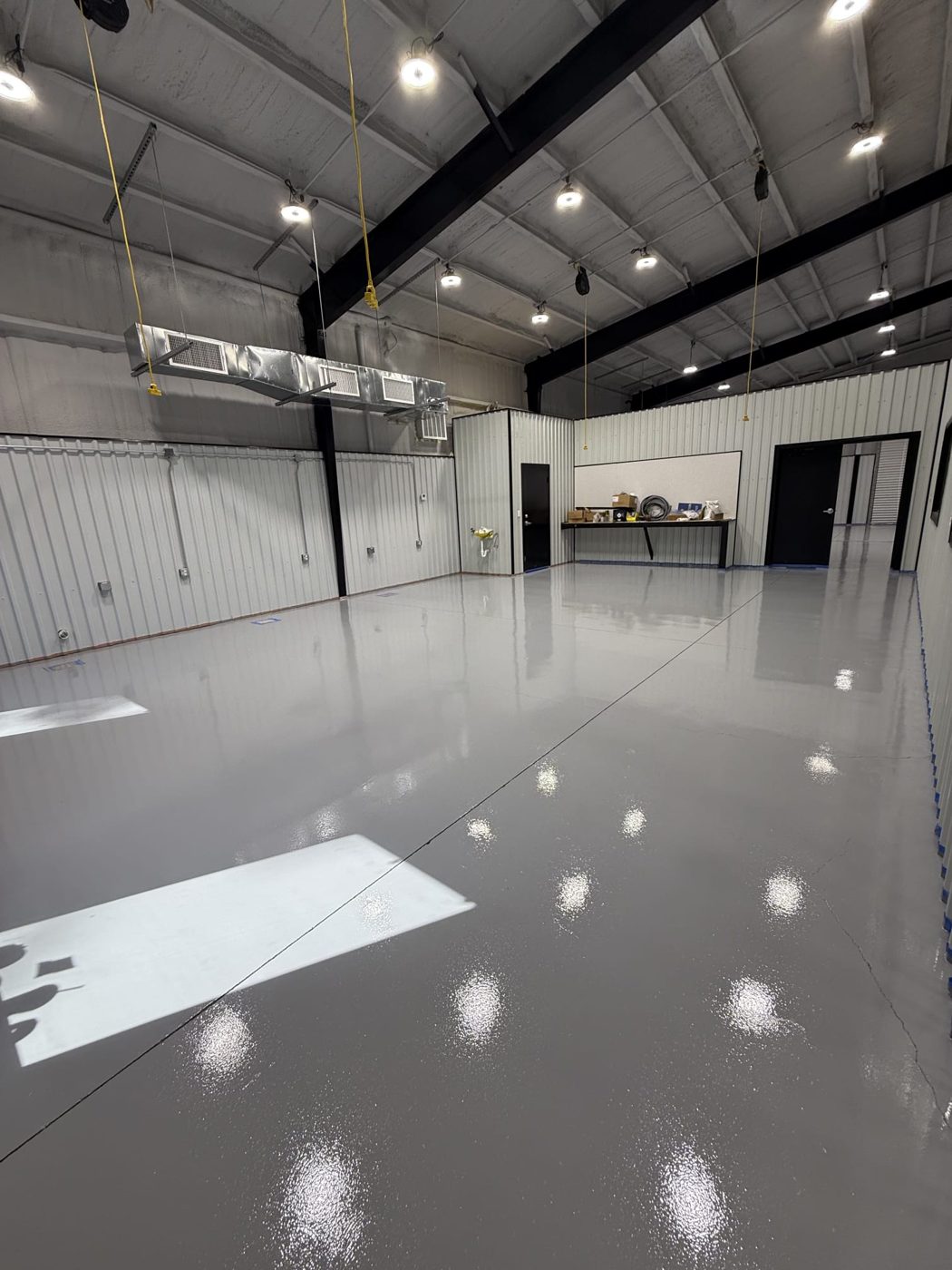Light gray high-gloss solid-color epoxy floor in a white metal-building shop with exposed steel beams by Signature Epoxy Flooring