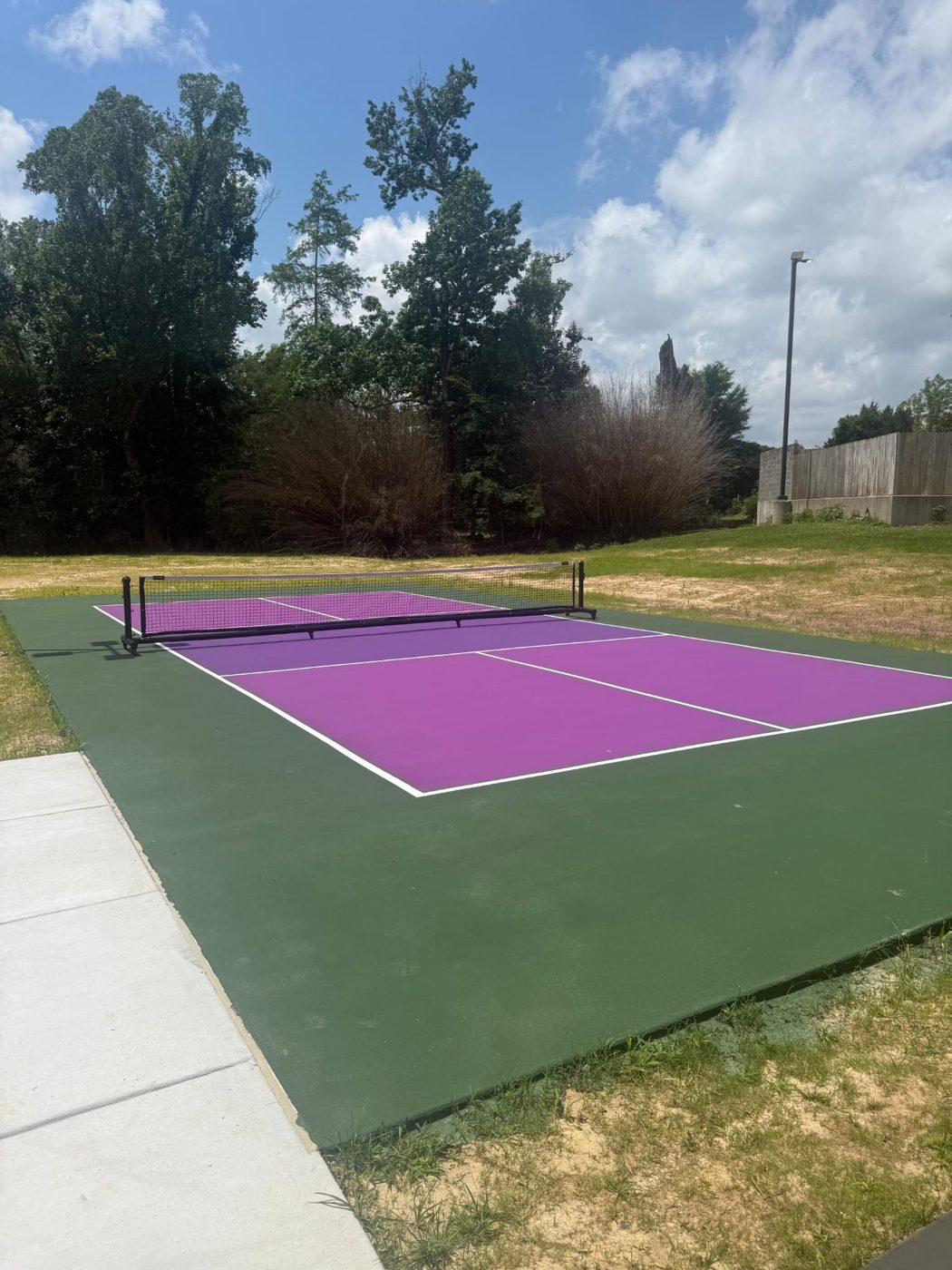 Freshly coated outdoor court with purple and green surfaces next to a concrete walkway in Zachary, LA