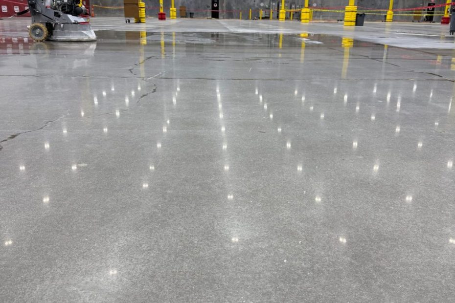 Polished concrete warehouse floor with yellow steel columns and overhead lights reflected